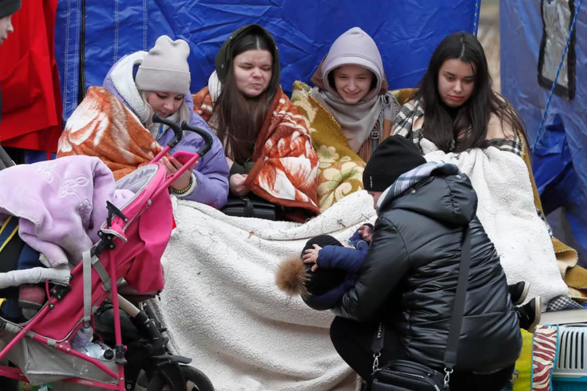 Refugiați ucraineni, acoperiți cu pături, se recuperează în fața unui cort după ce au trecut de punctul de trecere a frontierei româno-ucrainene din Siret, nordul României, 27 februarie 2022.