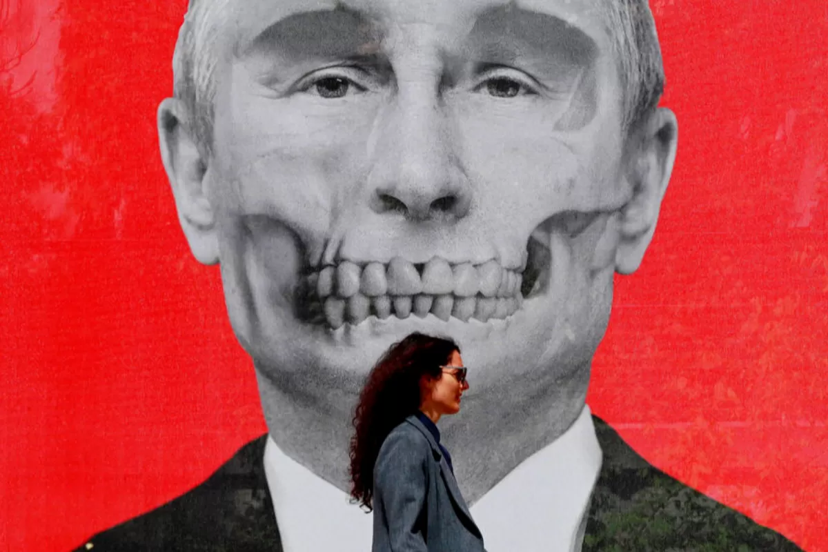 O româncă trece prin fața unui afiș care îl înfățișează pe președintele rus Vladimir Putin, parte a unei expoziții de artă anti-război din Piațeta Regelui, situată lângă complexul ambasadei Federației Ruse, la București, România, unde a fost lansată pe 29 aprilie 2022.