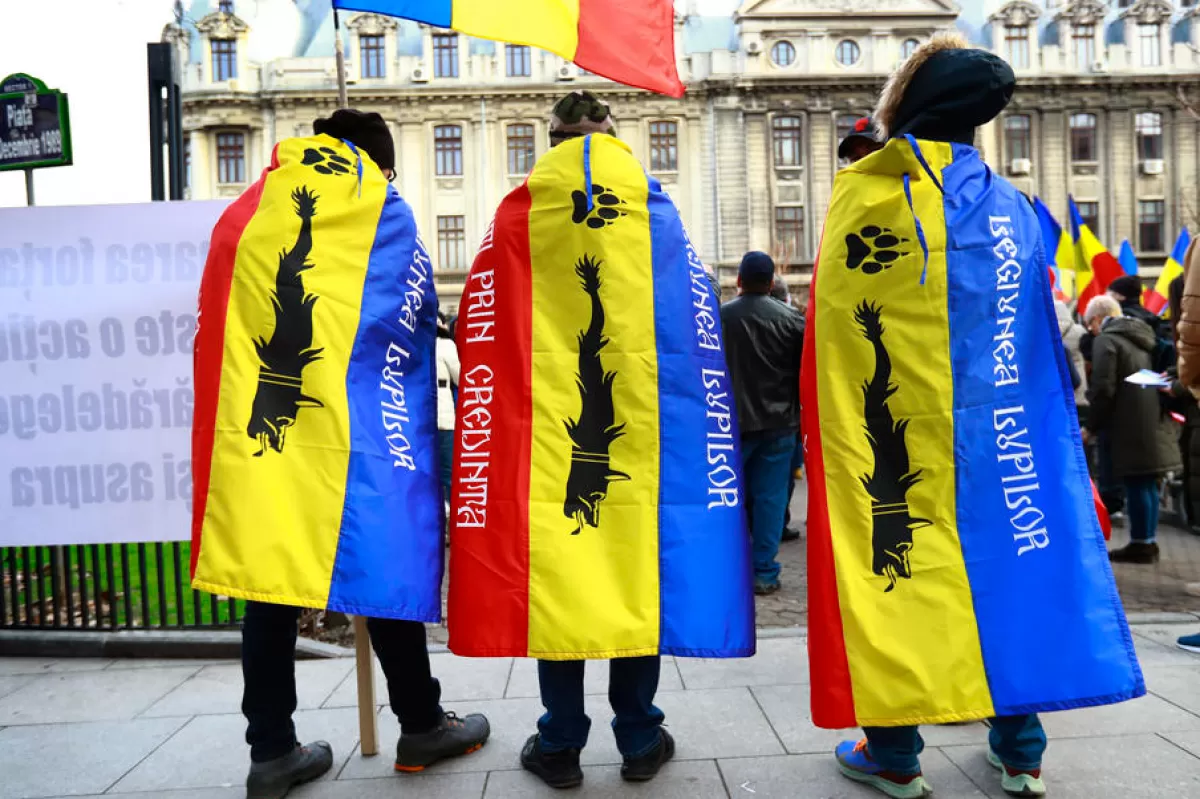 Трое молодых румынских националистов носят национальные флаги, на которых нарисованы черные волки, во время акции протеста против нового законопроекта об обязательной вакцинации и против новых мер, принятых румынским правительством во время третьей волны пандемии Covid-19, на Университетской площади в Бухаресте, Румыния, 20 марта 2021 года.