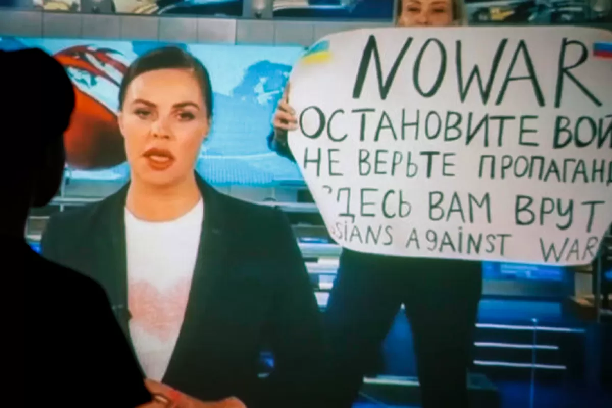 O femeie urmărește înregistrarea emisiunii de știri de seară de la postul de televiziune rus Canal Unu, în care o angajată intră în studioul TV din Ostankino cu un afiș pe care scrie „Fără război. Opriți războiul. Nu credeți propaganda. Aici sunteți mințiti” la Moscova, Rusia, 15 martie 2022.