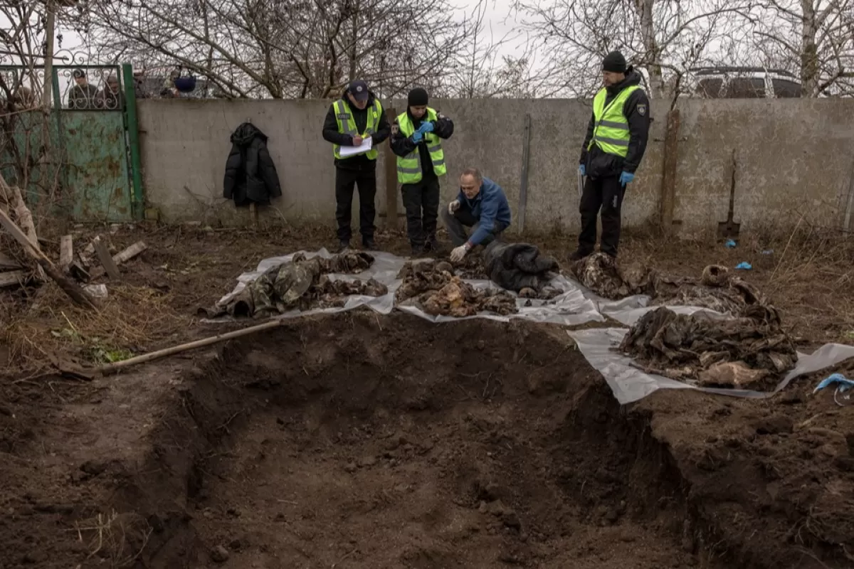 Судебно-медицинский эксперт Игорь Мотрич с сотрудниками полиции осматривают останки шести человек после их эксгумации из братской могилы во дворе села Правдыно под Херсоном, южная Украина, 28 ноября 2022 года