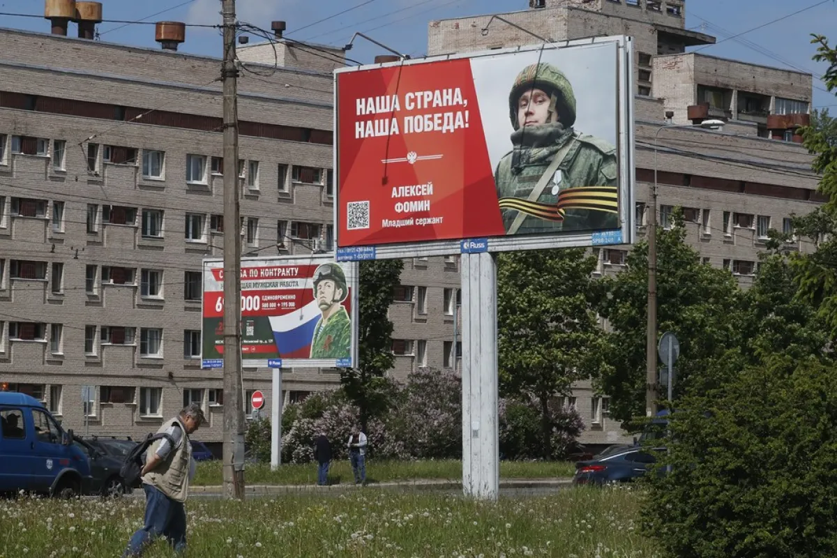 Un bărbat trece prin fața unor panouri înfățișând soldați și purtând sloganuri pe care scrie: „Serviciul militar cu contract. Slujba unui bărbat adevărat” și „Țara noastră, victoria noastră!”, în Sankt Petersburg, Rusia, 08 iunie 2023.