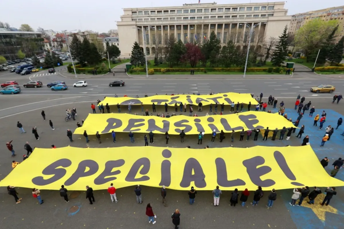 Voluntari români țin trei bannere galbene în timpul unui protest împotriva pensiilor speciale desfășurat în fața sediului guvernului (în fundal), la București, România, 07 aprilie 2023.