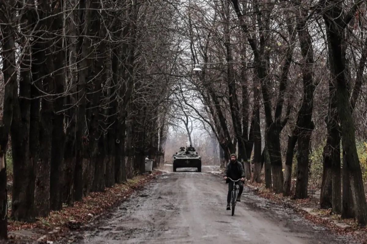 Un bărbat circulă cu bicicleta în timp ce un vehicul de infanterie militară trece prin Chasiv Yar, lângă linia frontului în regiunea Donețk, Ucraina, 9 noiembrie 2023, pe fondul invaziei ruse.